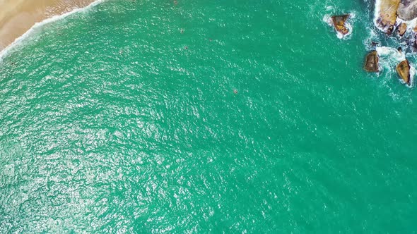 People swim and snorkel on turquoise lagoon with vibrant water reflecting sunlight, white waves spla alt