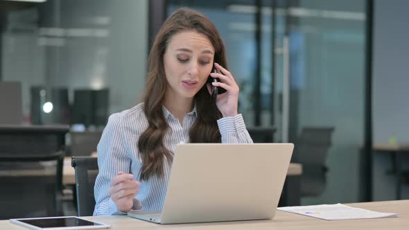 Young Businesswoman Talking on Smartphone while using Laptop alt