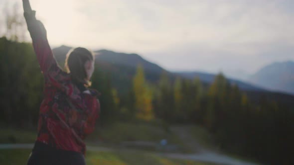 Slow motion of a young woman dancing on a wooden platform at sun set, golden hour. Alpine mountains alt