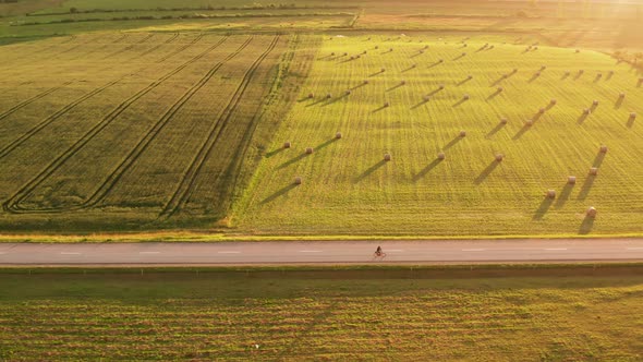 Person cycling on country roads through rural farmland, sunset aerial view alt