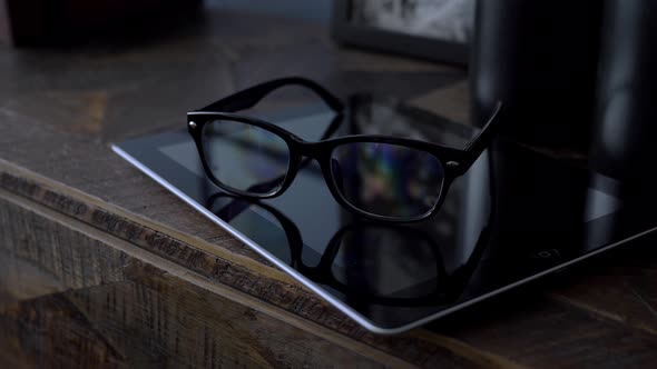 Glasses in Black Rim Lying on a Tablet on a Wooden Dresser in the Room Close Up alt