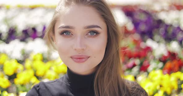 Beautiful Female with Blue Eyes and Makeup Posing on Blurred Background of Colorful Flowers alt