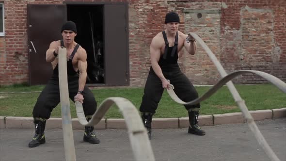 Two Young Muscular Men Training and Do Crossfit Exercises with Battle Ropes. The Camera Zooms in alt