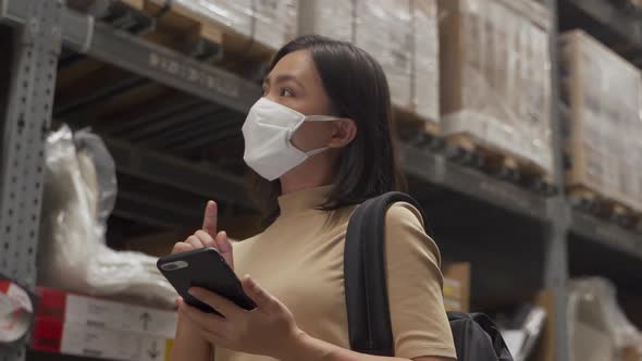 Asian woman wearing mask walking in warehouse and use smart phone.