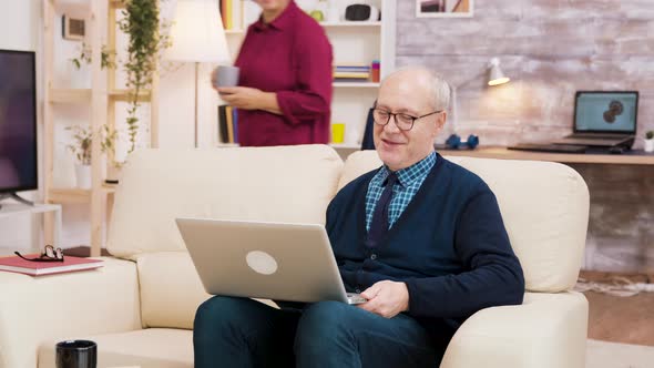 Elderly Age Couple with Glasses Sitting on Sofa During a Video Call on Laptop alt