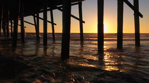 Panning view of sunset under pier as waves roll into the beach alt