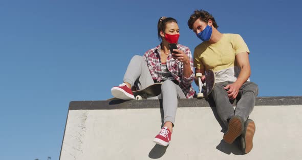 Caucasian woman and man friends wearing face mask, sitting and using smartphone alt