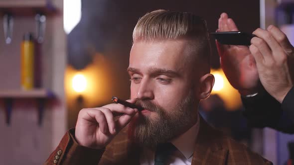 Hairstylist Does Hair Styling Hair to Businessman Smoking in Salon