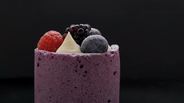 Beautiful mousse cake with fresh berries rotating on black plate alt
