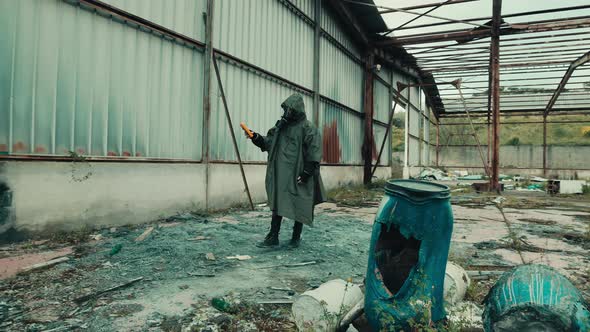 Man with Gas Mask Checks the Radiation Level with the Geiger Counter in a Shed alt