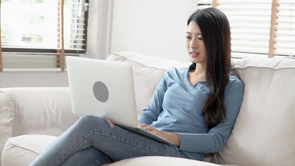 Young asian woman working online laptop with smile and happy sitting on couch at living room. alt