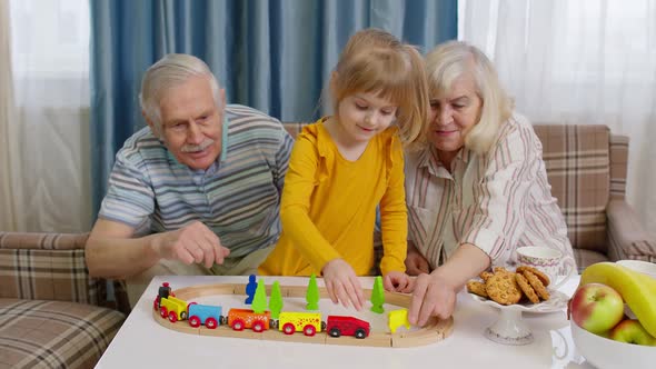 Mature Couple Grandmother Grandfather with Child Girl Grandkid Riding Toy Train on Railroad at Home alt