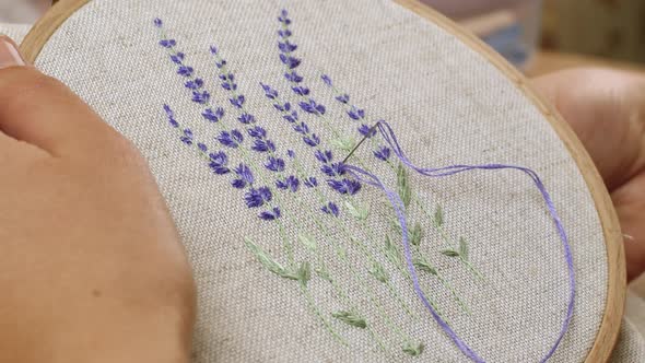 Woman embroiders very beautiful lavender flowers on linen fabric. Handmade embroidery, art, woman