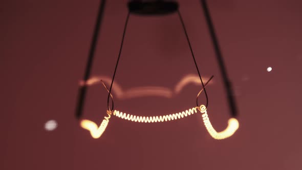 The Tungsten Filament in a Glass Lamp Closeup in Slow Motion on Red Background alt