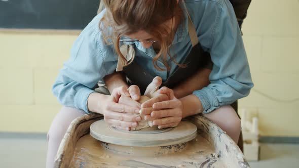 Man and Woman Making Pot on Throwing Wheel Shaping Clay Together in Workshop alt