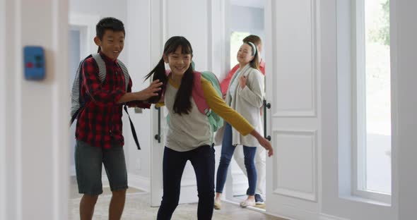 Excited asian son and daughter running through front door, returning home with parents alt