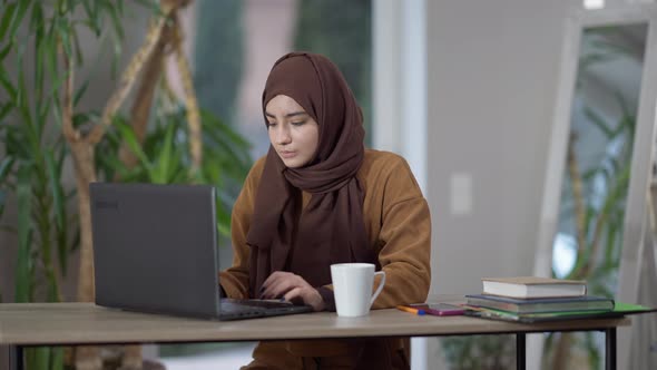 Overworked Woman in Hijab Closing Laptop Sighing and Rubbing Temples alt
