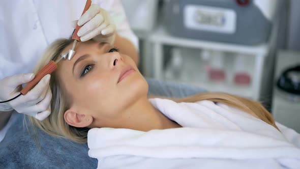 Closeup of Beautiful Woman Receiving Facial Microcurrent Treatment From Therapist at Beaty Salon alt