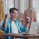 Happy Asian Male Designer Working On A Laptop And Celebrating And Dancing While Designing Clothes - VideoHive Item for Sale