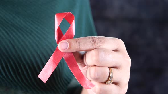 Women Hand Holding Red HIV Ribbon Isolated on Black alt