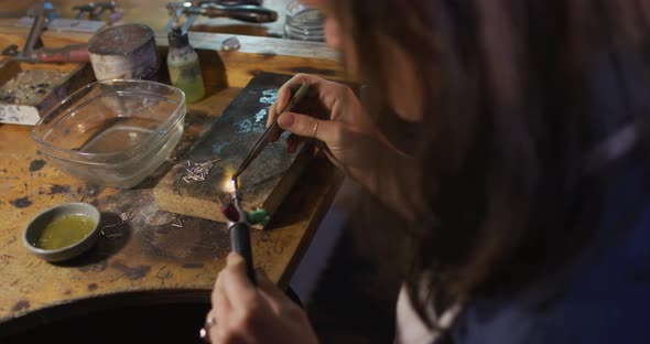 Close up of caucasian female jeweller sitting at desk, making jewelry in workshop alt