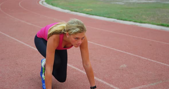 Front view of Caucasian female athlete taking starting position and running on a track at sports ven alt
