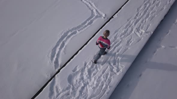 Overhead view of young blonde girl slowly and casually wandering around a frozen lake. alt
