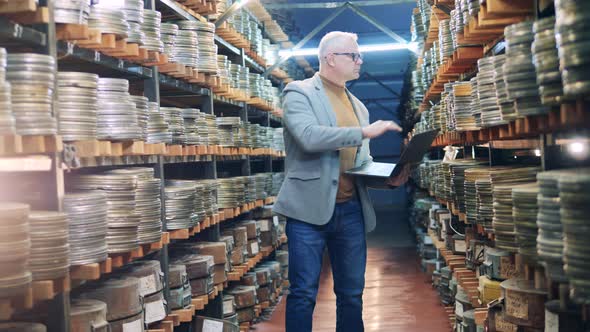 Archive Specialist with a Laptop is Observing Cases with Film Tape alt