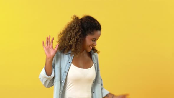 Happy young cheerful African American woman smiling and dancing on yellow studio background