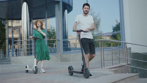 Happy Couple Walks Down Stairs with Electric Scooters on City Area in Summer alt