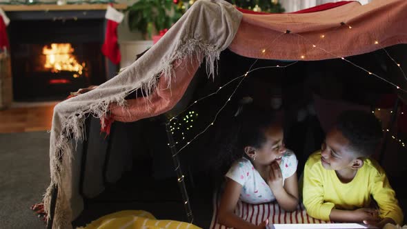 Happy african american siblings using tablet in makeshift tent alt