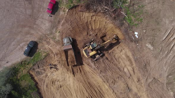 Top aerial shot: tractor bucket is filling a truck body. 