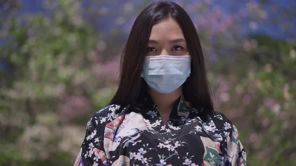 Live Camera Zoom in to Serious Asian Young Woman in Kimono and Coronavirus Face Mask Looking at alt