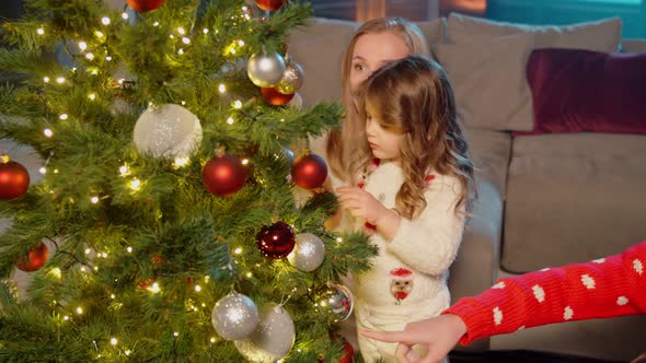 Two Sisters and Their Mother Decorating Christmas Tree alt