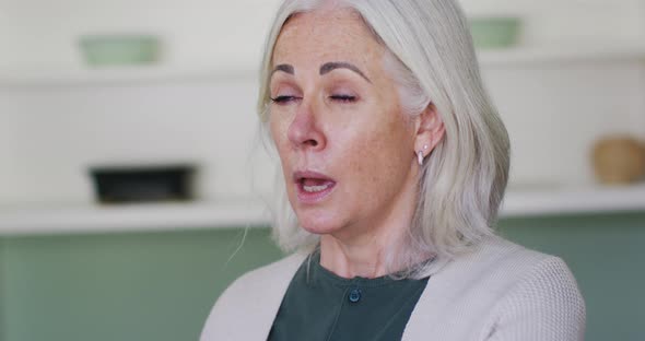Portrait of senior caucasian woman coughing or sneezing into her arm alt