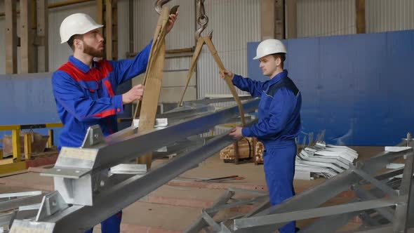 Workers at the Plant Load the Cargo Onto the Hook of the Crane Against the Background of Production alt