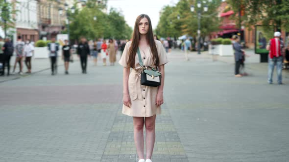 Zoomin Time Lapse of Attractive Young Lady Standing Outdoors in Busy Street and Looking at Camera alt