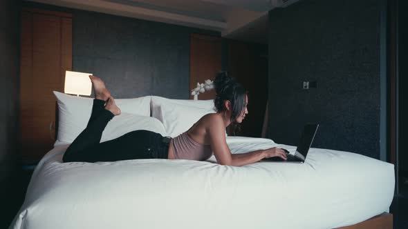 Woman Freelancer with Computer Lying on a Bed in Hotel Room alt