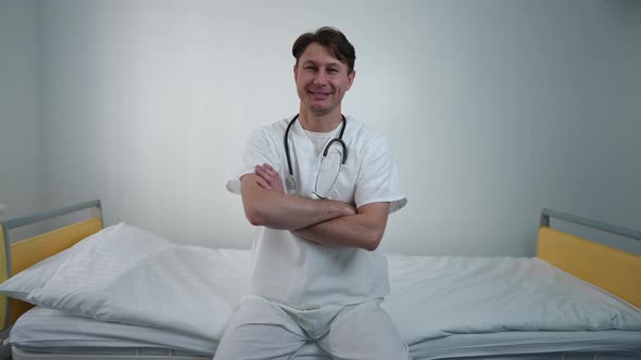 Portrait of Confident Doctor Crossing Hands Looking at Camera Smiling Sitting on Bed in Comfortable alt