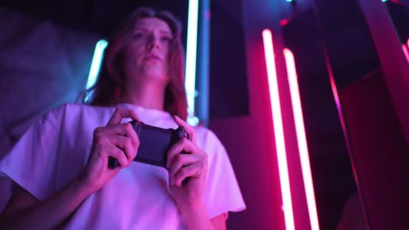 A Female Gamer Plays a Computer Game on a Black Joystick in the Light of Neon