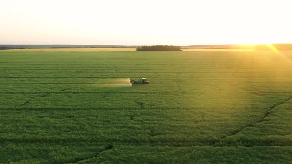 Farmer Tractor Sprays Fertilizers Over Field Of Agricultural Crops At Sunset alt