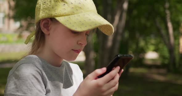 Little Girl Playing the Game on Her Smartphone While Sitting Outdoors alt
