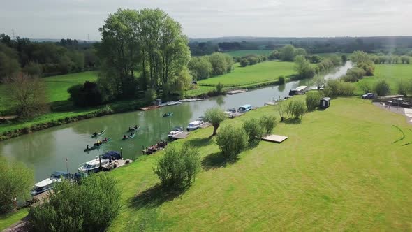 Boats Moored On The Edge Of River Thames With People Kayaking On The Water Surrounded In Green Natur alt