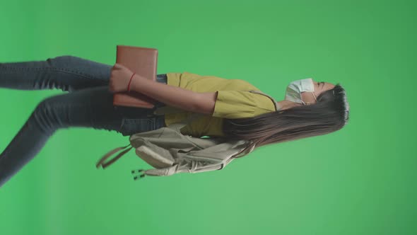 Side View Of Asian Girl Student Wearing A Mask, Holding Book While Walking To School On Green Scree alt