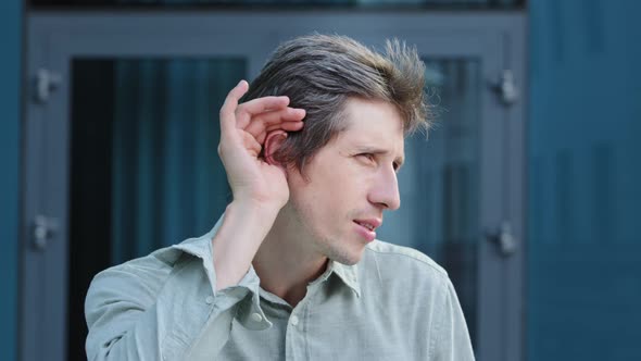 Positive Young Caucasian Male Professional Hold Hand Near Ear Trying to Hear Whisper Something alt