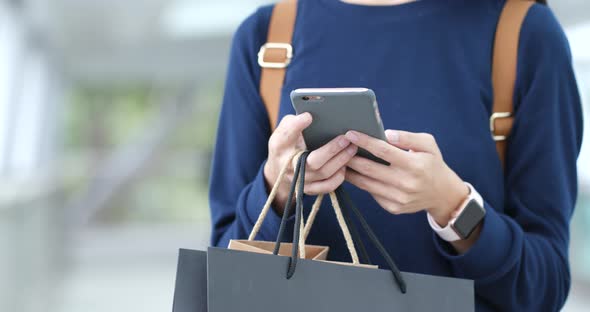 Woman use of mobile phone at outdoor and holding paper bag alt
