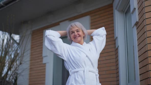 Excited Slim Beautiful Mature Woman Stretching Standing on Porch Outdoors Smiling alt