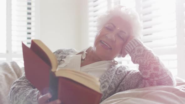 African american senior woman smiling while reading a book sitting on a bean bag at home alt