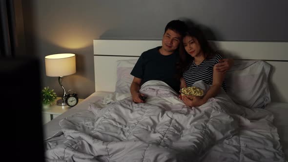 happy young couple watching TV on a bed at night