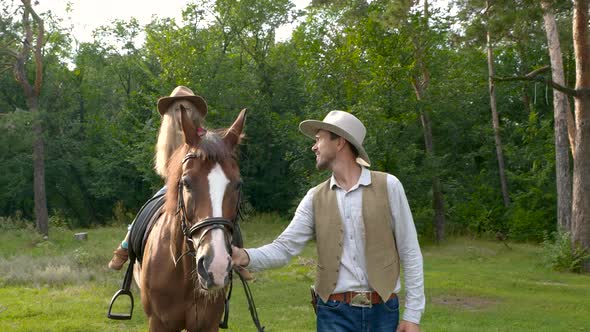 A Young Cowboy is Leading a Horse on Which His Daughter is Sitting alt